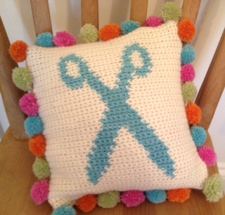 Crochet cushion with scissor image and pom poms